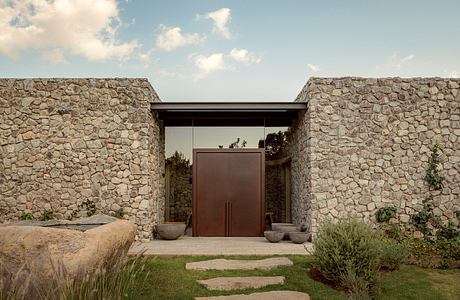 A rustic stone entryway with a modern wooden doorway, surrounded by lush landscaping.