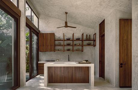 A minimalist kitchen interior with wooden shelves, a concrete countertop, and a ceiling fan.