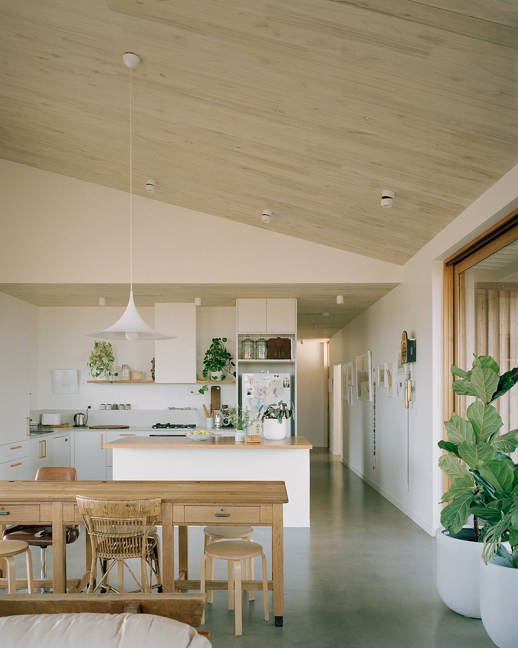 A warm, light-filled kitchen with a wooden ceiling and minimalist decor. Natural materials and greenery create a cozy atmosphere.