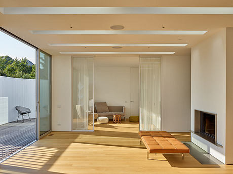 Bright, minimalist living room with wooden floors, recessed lighting, and sliding glass doors.