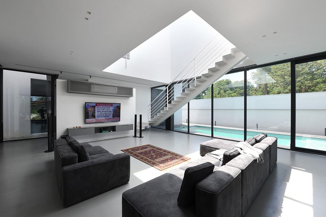 Modern open-plan living space with sleek staircase, large window, and pool view.