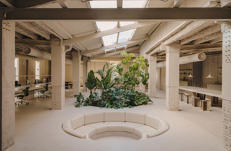 Lush indoor garden with curving sofa and exposed brick walls, showcasing modern office design.