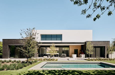 A modern, single-story home with a flat roof, large windows, and a pool in the foreground.