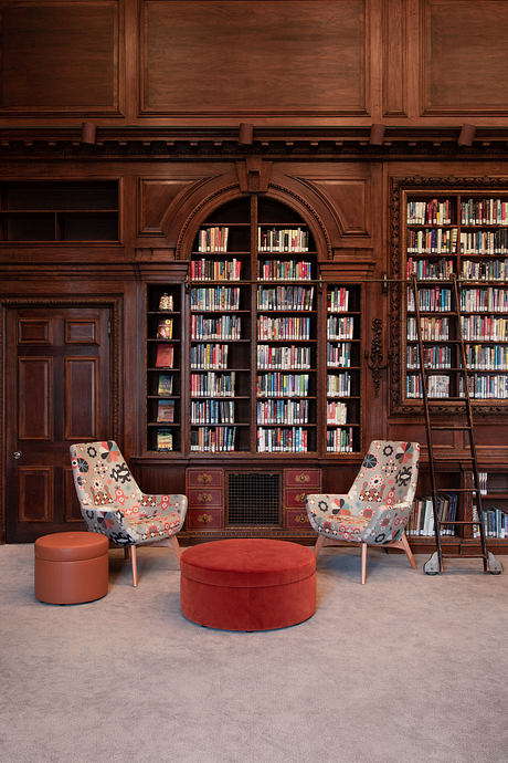 Ornate wooden bookshelves, patterned chairs, and plush red ottomans in a cozy library.