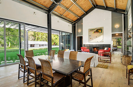 A bright, modern interior with an open-plan layout, wood-beamed ceiling, and floor-to-ceiling windows.