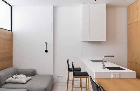 Minimalist, open-concept kitchen with sleek white countertop and wood accents.