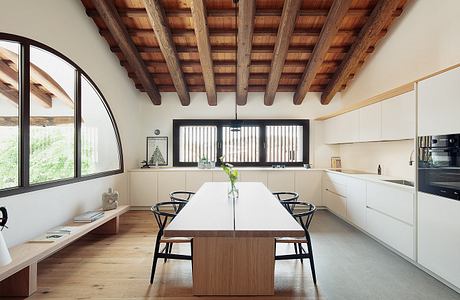 Modern kitchen with wooden beamed ceiling, large windows, and minimalist furniture.