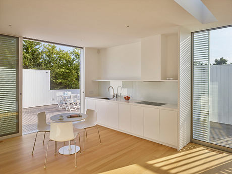A modern, open-concept kitchen with sleek white cabinetry, minimalist decor, and large windows offering abundant natural light.