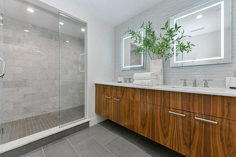 A modern bathroom with a sleek marble shower, wooden vanity, and potted plant accents.