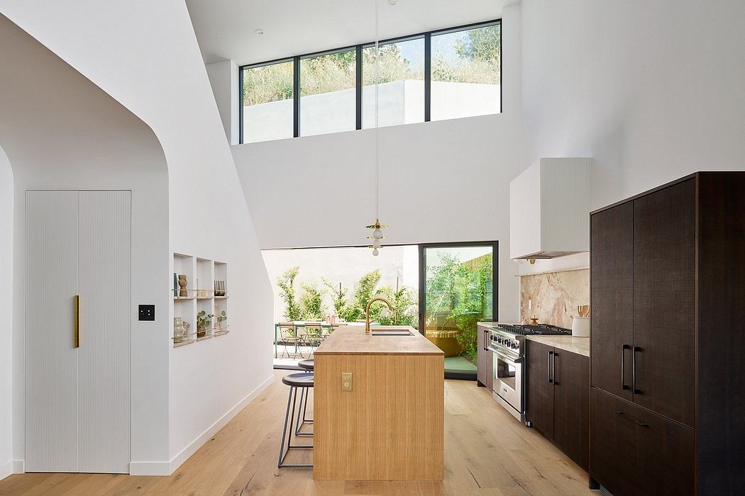 Modern kitchen with wood floors, island, and large windows overlooking greenery.
