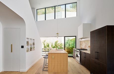 Modern kitchen with wood floors, island, and large windows overlooking greenery.