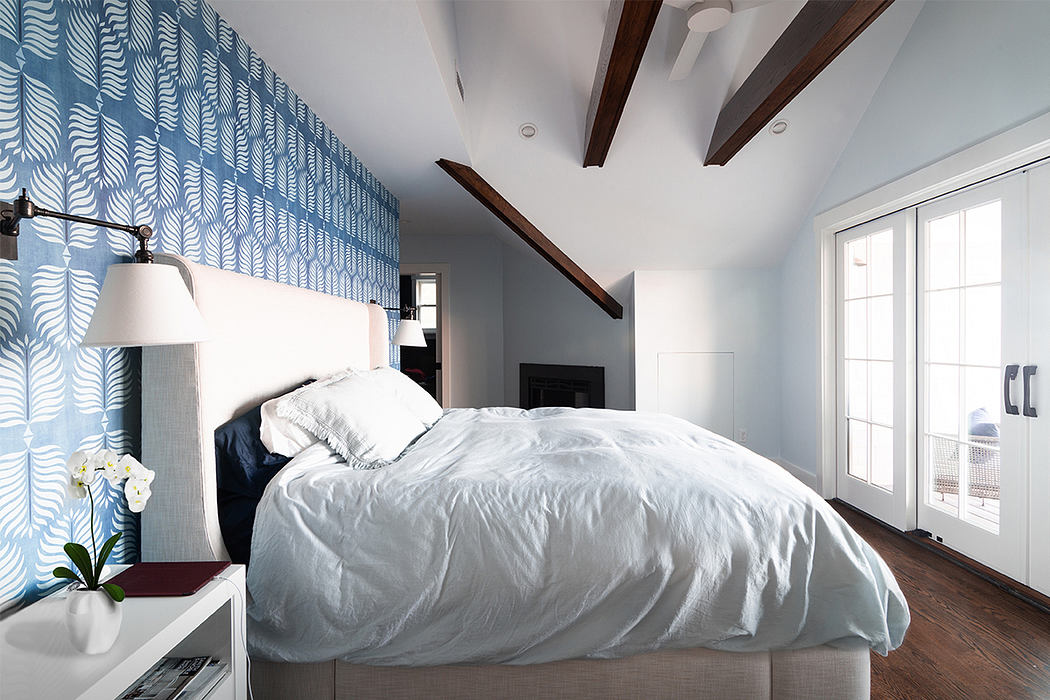 A modern bedroom with a patterned blue feature wall, wooden beams, and large windows.