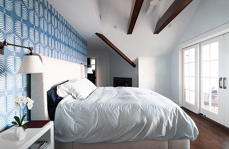 A modern bedroom with a patterned blue feature wall, wooden beams, and large windows.