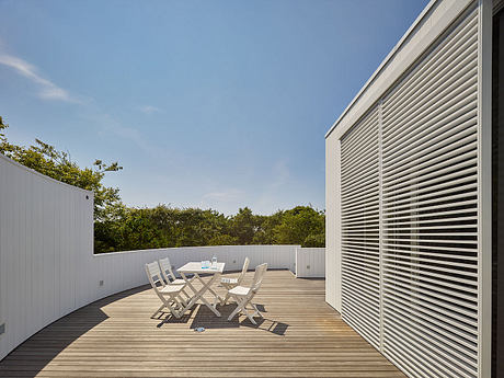 Expansive outdoor deck with slatted walls, offering a tranquil dining area amidst lush foliage.