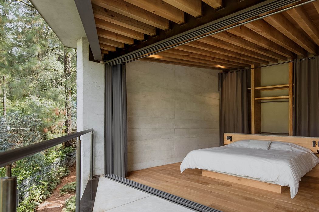 Minimalist bedroom with wooden beams, concrete walls, and large glass windows overlooking nature.