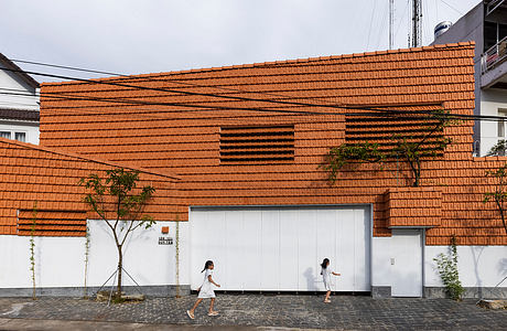 A modern brick building with distinctive angled roofing and two people walking on the pavement in front.