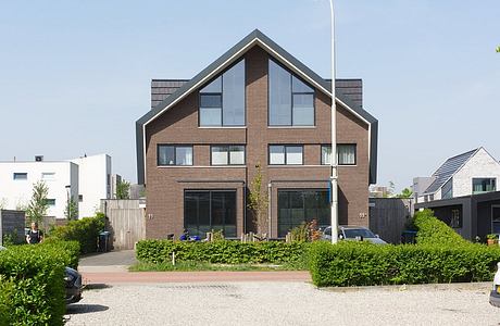 Modern two-story brick building with triangular roof and large windows, surrounded by greenery.