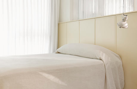 A minimalist bedroom with clean lines, beige tones, and a floor-to-ceiling window providing ample natural light.