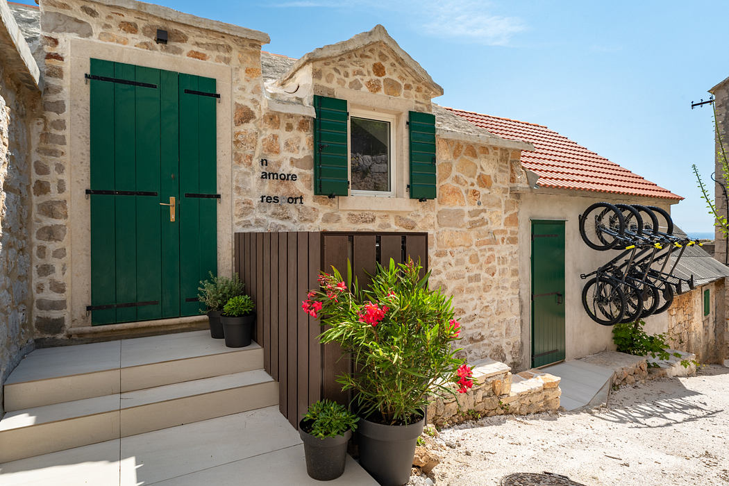 Charming stone cottage with green shutters, potted plants, and a bike rack on the patio.
