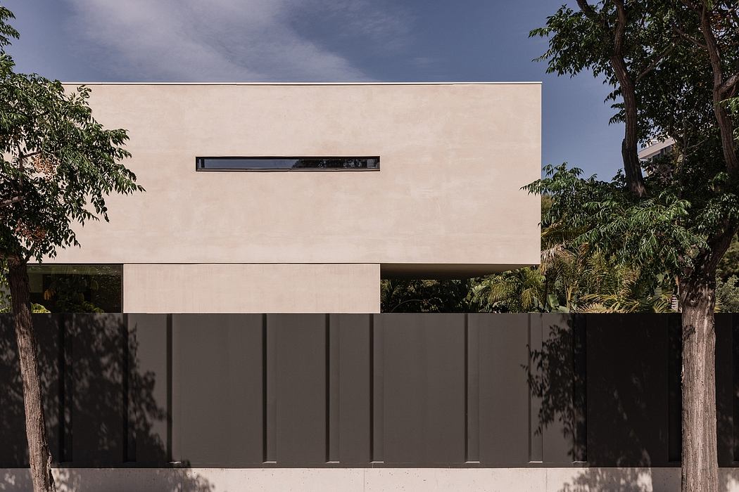 A minimalist, sleek beige exterior with a long horizontal window and lush foliage surrounding it.