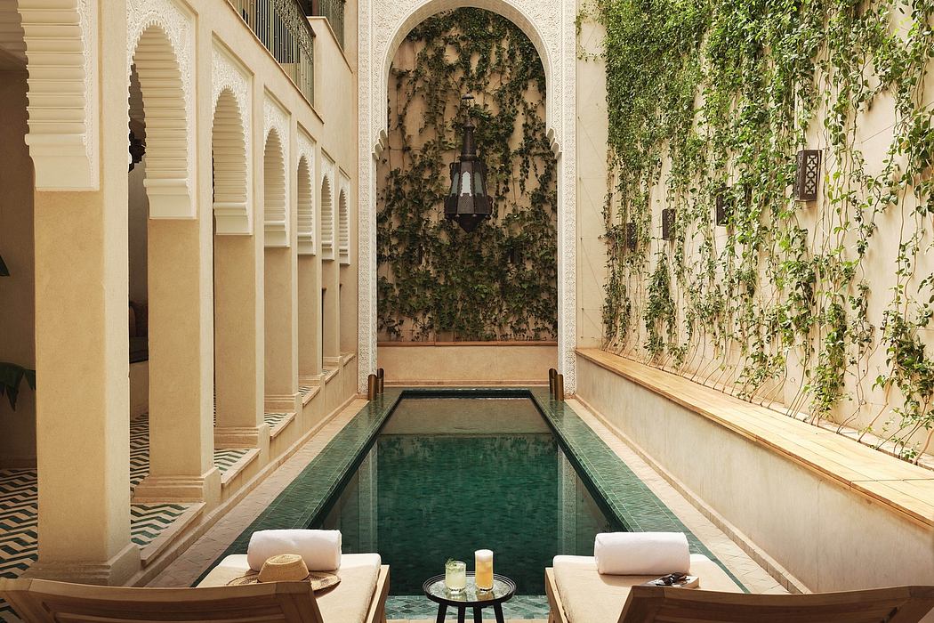 An ornate Moroccan-style indoor pool surrounded by lush greenery and intricate architectural details.