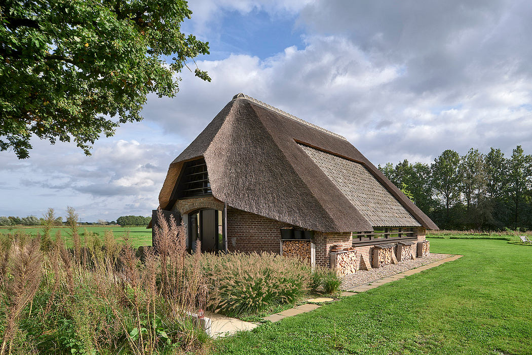A rural barn with a distinctive thatched roof, surrounded by lush greenery and a grassy field.
