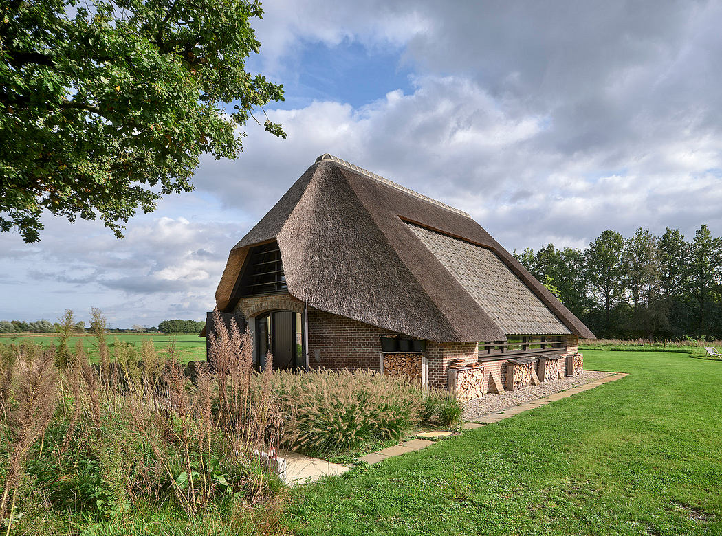 A rural barn with a distinctive thatched roof, surrounded by lush greenery and a grassy field.