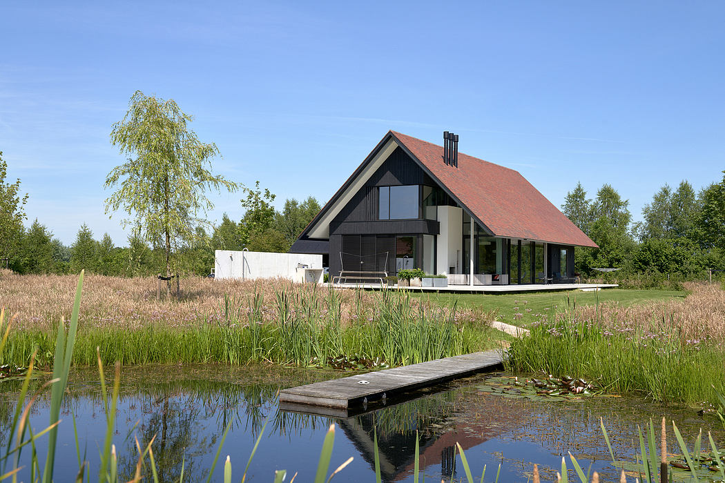 A modern chalet-style house with a red tiled roof, large windows, and a tranquil pond in the foreground.
