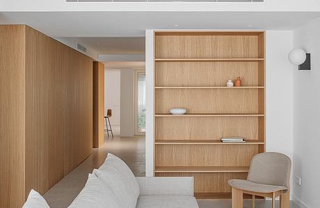 Minimalist living room with wooden shelving unit, concrete floors, and neutral furniture.