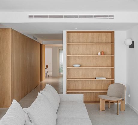 Minimalist living room with wooden shelving unit, concrete floors, and neutral furniture.