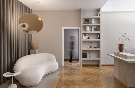 Minimalist living room with curved sofa, wooden shelving, and decorative lighting.