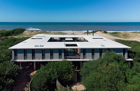 A modern beach house on stilts with a deck overlooking the ocean horizon.