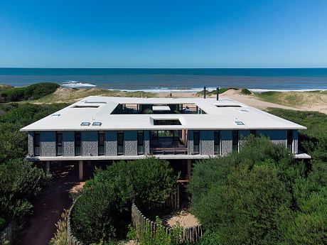 A modern beach house on stilts with a deck overlooking the ocean horizon.