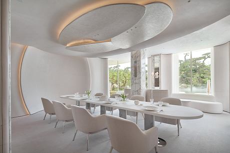 Elegant modern dining room with curved ceiling, large windows, and minimalist furnishings.