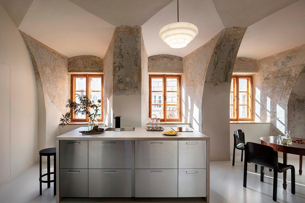 A modern, minimalist kitchen with stone arched walls, large windows, and sleek gray cabinets.
