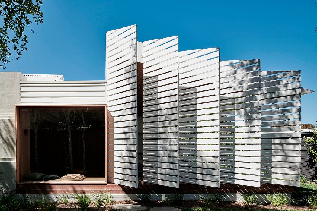 A modern, white, angled facade with a wooden doorway and patio leading to an interior courtyard.