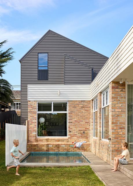 Modern home with a gabled roof, brick facade, and small pool on a grassy lawn.