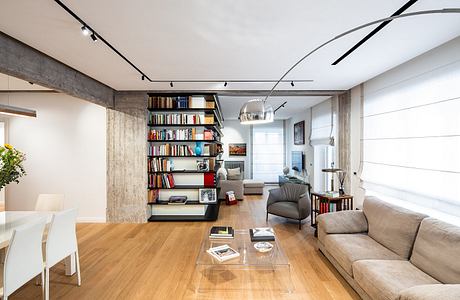 Modern open-plan living space with bookshelf, track lighting, and minimalist furniture.