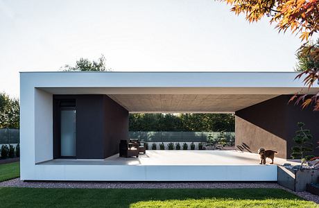 A modern, minimalist pavilion with clean lines, a flat roof, and glass walls overlooking a lush garden.