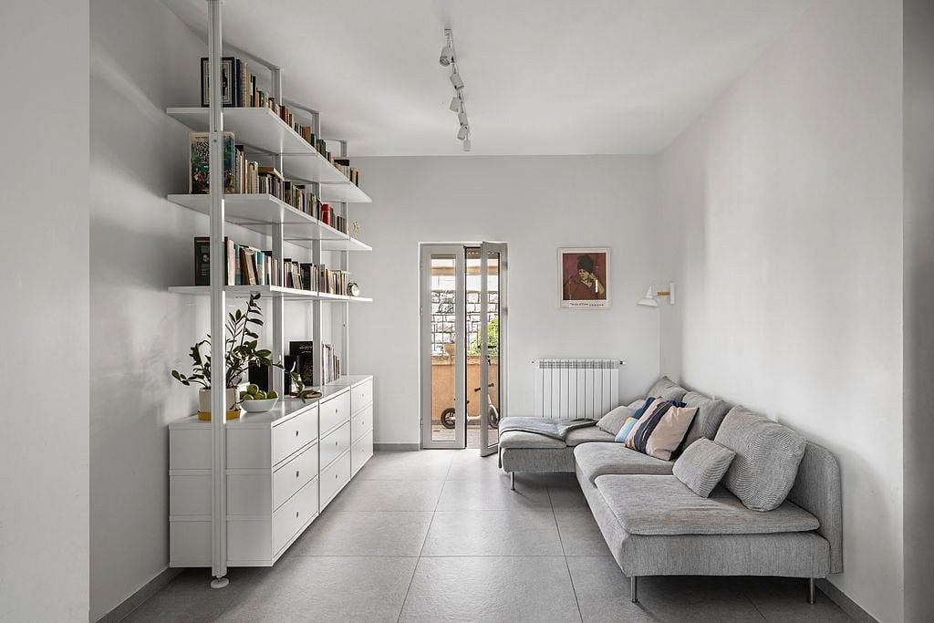 The room features modern shelving, a gray sectional sofa, and a minimalist decor style.