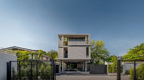 A modern, three-story concrete building with a covered garage and lush greenery.