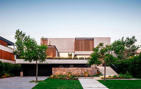 A modern, multi-level building with stone foundation, wood and concrete accents, and lush landscaping.