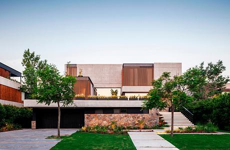 A modern, multi-level building with stone foundation, wood and concrete accents, and lush landscaping.