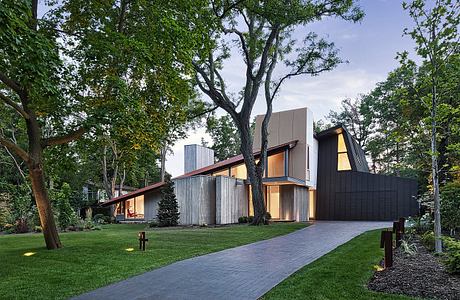 Sleek, modern home with wood and glass exterior, surrounded by lush foliage.