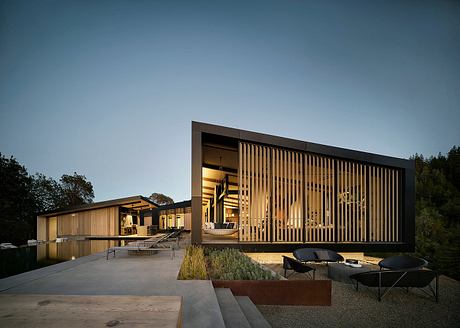 A modern, wooden-paneled building with a geometric facade and a reflecting pool in the foreground.