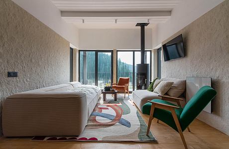 Modern, cozy living room with wooden floor, large windows, fireplace, and colorful rug.