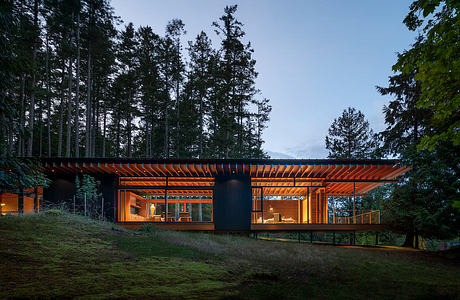 A modern, wooden structure nestled in a forested landscape, featuring large windows and a cantilevered roofline.