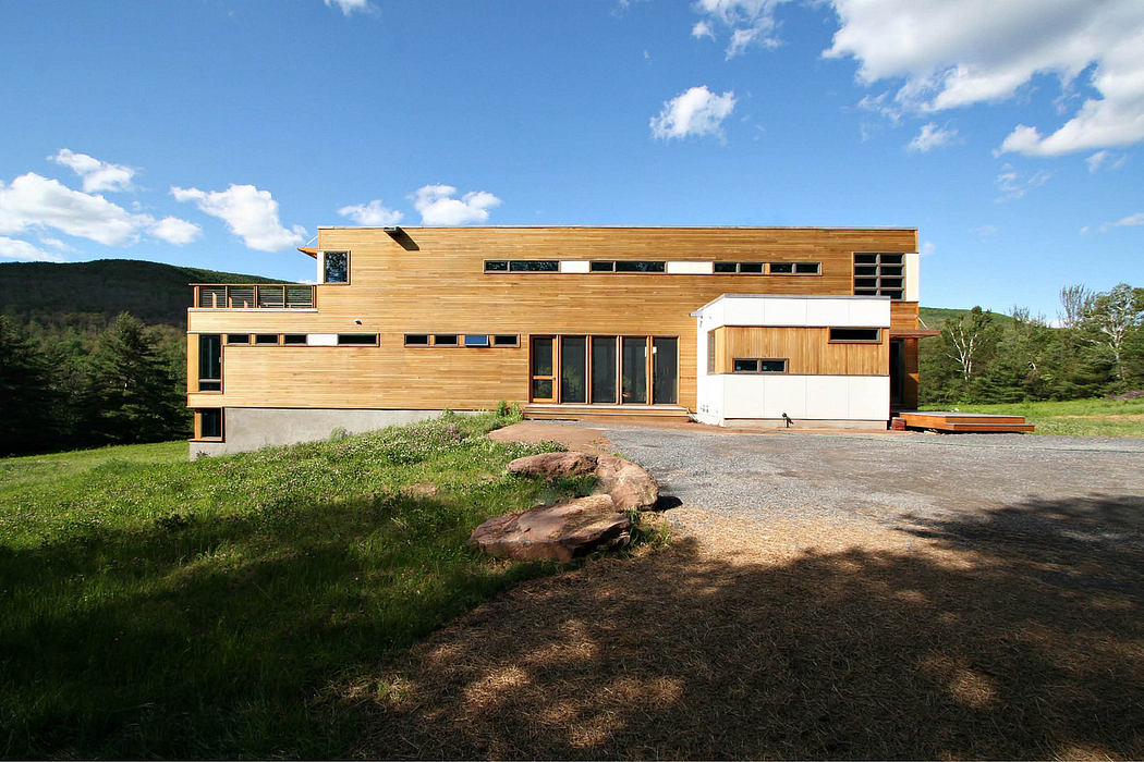Modern, eco-friendly home with wood exterior, large windows, and outdoor deck overlooking hills.