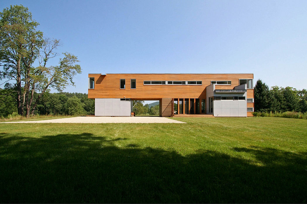 A modern, wood-paneled home set against a lush, grassy backdrop with large windows and a garage.