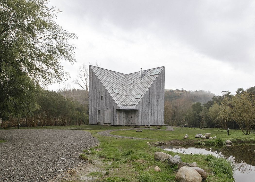 A modern angular wooden structure surrounded by a pond and lush vegetation.